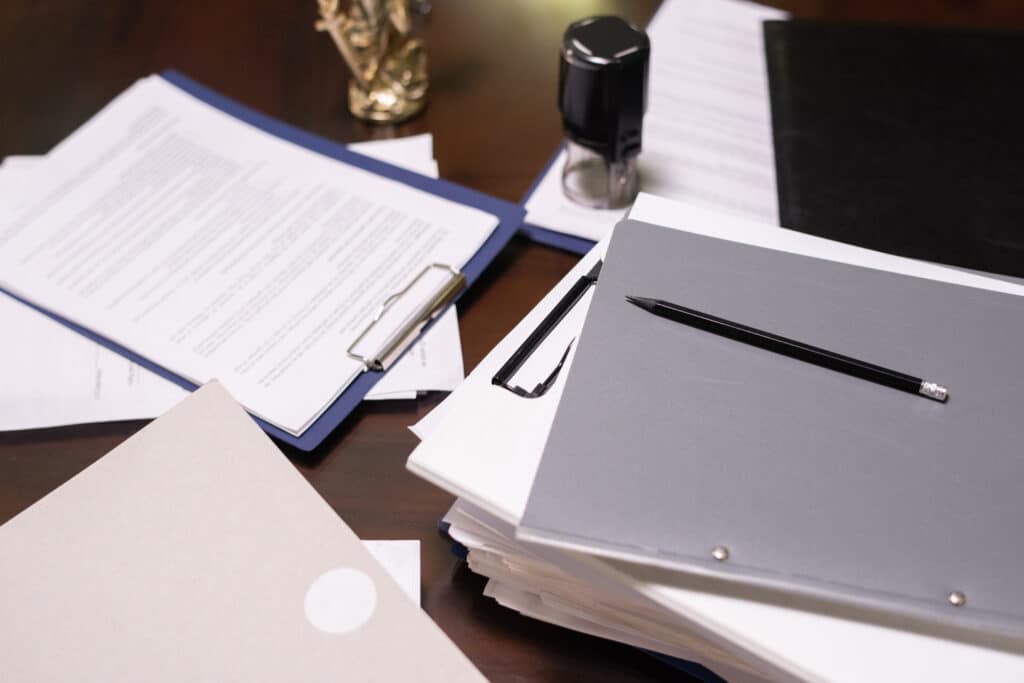 Teil eines Tisches mit Stapeln juristischer und geschäftlicher Dokumente in Ordnern und Klemmbrettern mit Bleistift darauf